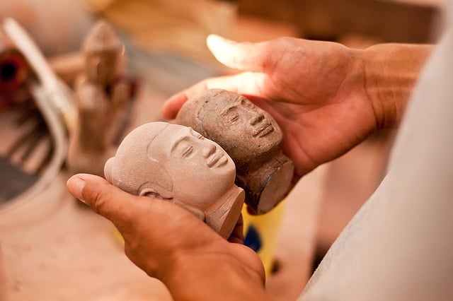 Two stonemasons carefully carving intricate details into a large slab of granite in a workshop.